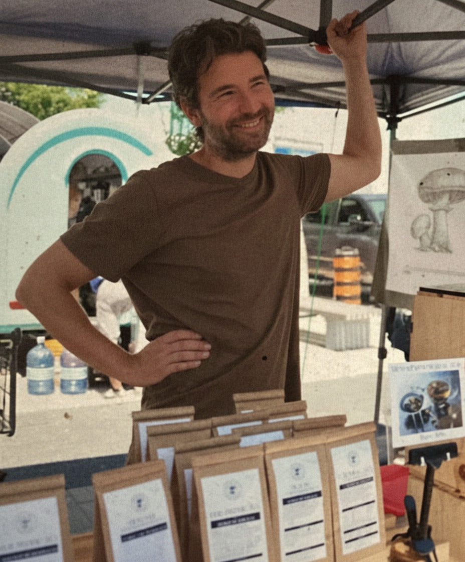Man standing behind a wooden display with menus at an outdoor event.